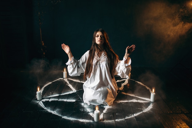 Foto strega in camicia bianca seduta al centro del cerchio del pentagramma con candele, rito occulto, evocazione di spiriti. occultismo ed esorcismo