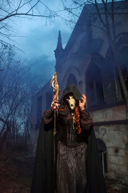 a witch with red hair in a black cloak with a staff at night against the backdrop of an old castle