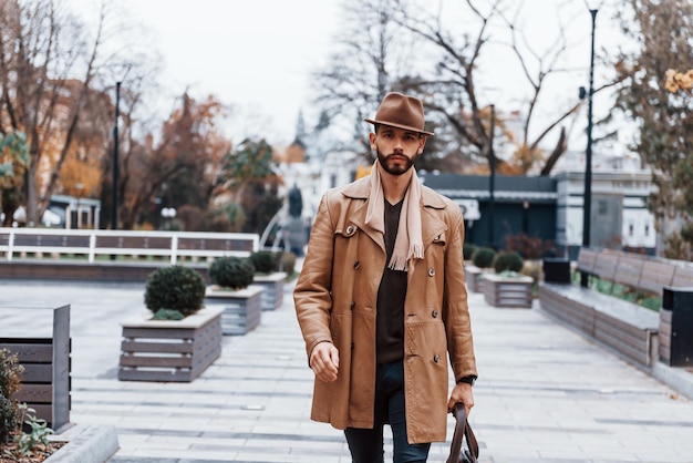 With bag Young male model in fashionable clothes is outdoors in the city at daytime