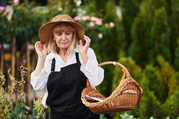 手にバスケットを持って年配の女性は日中に庭にいます植物と季節の概念