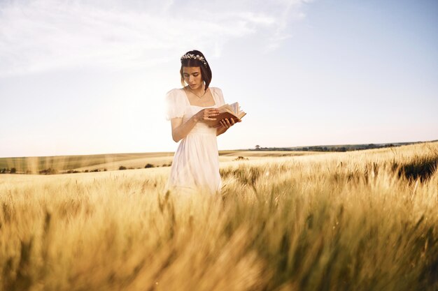 手に本を持って 白いドレスを着た美しい若い花嫁は、晴れた日に農業分野にいます