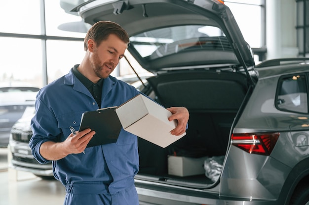 Photo with box and notepad man in blue uniform is working in the car service