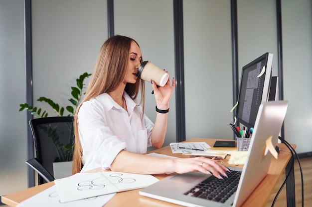 コーヒーを飲みながらフォーマルな服を着た若い大人の女性がオフィスの屋内にいます