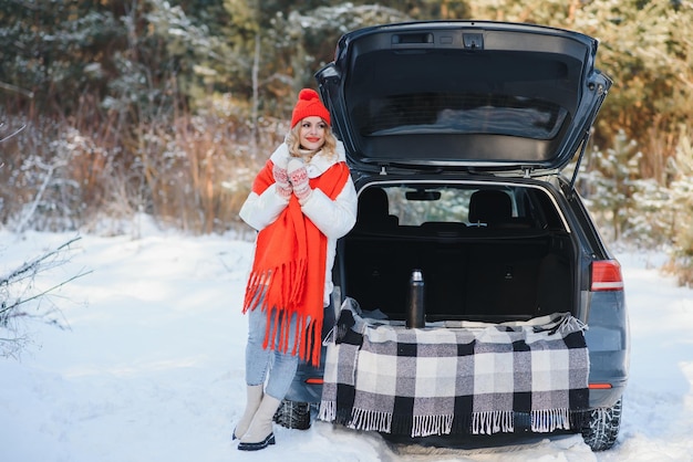 写真 一杯の飲み物と 美しい若い女性は屋外で冬の時間に彼女の自動車の近くにいます