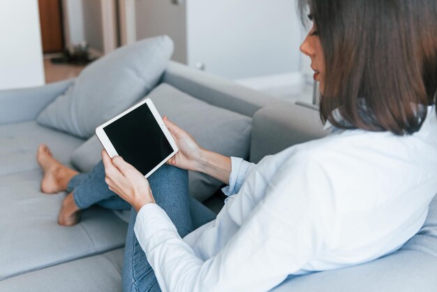 With digital tablet in hands Young woman is indoors in room of modern house at daytime