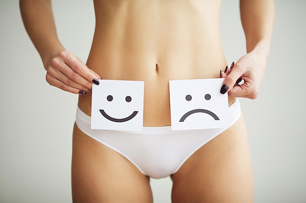 With fit slim body in panties holding white card with sad smiley face near her stomach