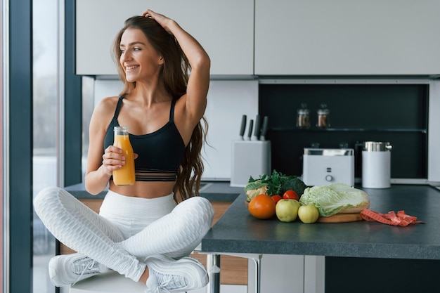 With fresh orange juice Young european woman is indoors at kitchen indoors with healthy food