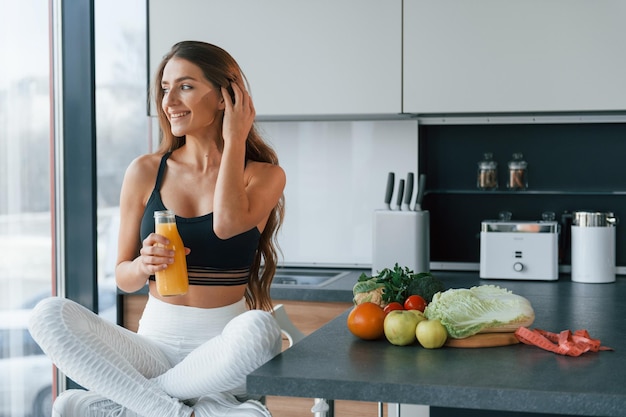 新鮮なオレンジジュースで若いヨーロッパの女性は健康的な食べ物で屋内のキッチンで屋内にいます