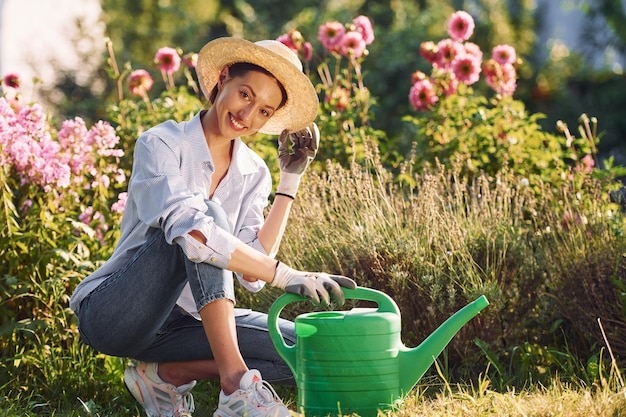 緑の水缶と若い陽気な女性が昼間庭にいる