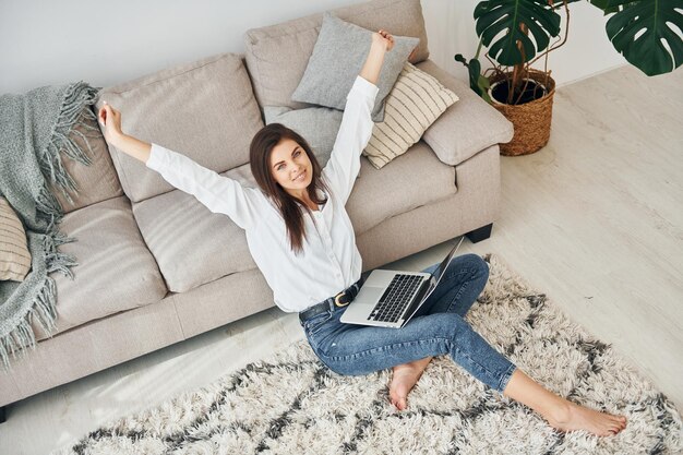 With laptop Beautiful young woman in jeans and white shirt is at home