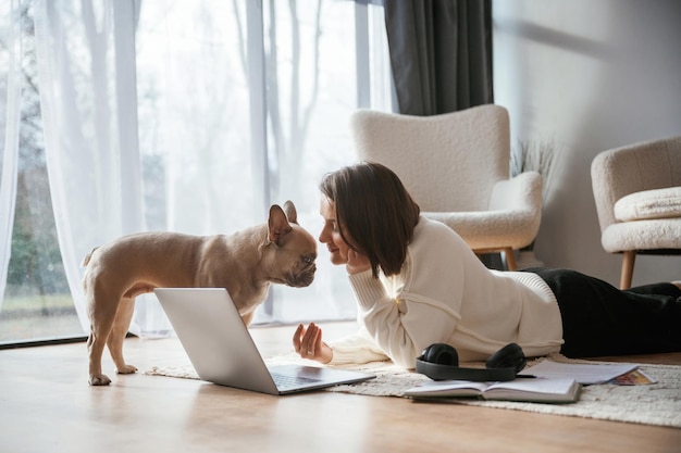 With laptop On the floor Young woman is with her pug dog at home