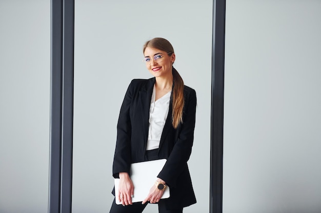 With laptop Young adult woman in formal clothes is indoors in the office