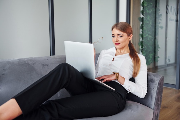 With laptop Young woman in formal clothes is indoors on the sofa at daytime