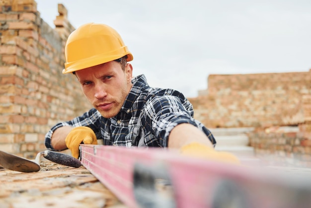 Foto con lo strumento di misurazione del livello il lavoratore edile in uniforme e le attrezzature di sicurezza hanno un lavoro sulla costruzione