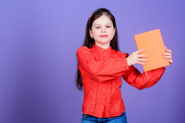 With a library you are free cute small child holding library\
book with orange cover adorable little girl borrowing book in\
library reading in a school library copy space