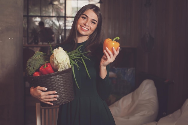 With lots of vegetables in basket beautiful woman is standing