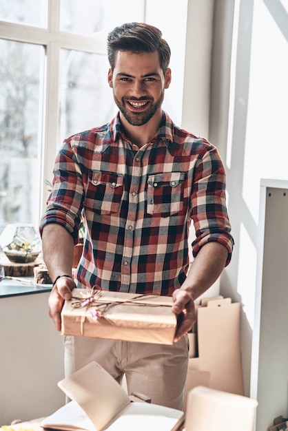 Con amore per te. bel giovane che dà una confezione regalo e guarda la telecamera con un sorriso