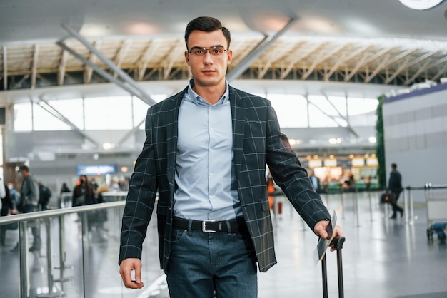 With lugagge Young businessman in formal clothes is in the airport at daytime