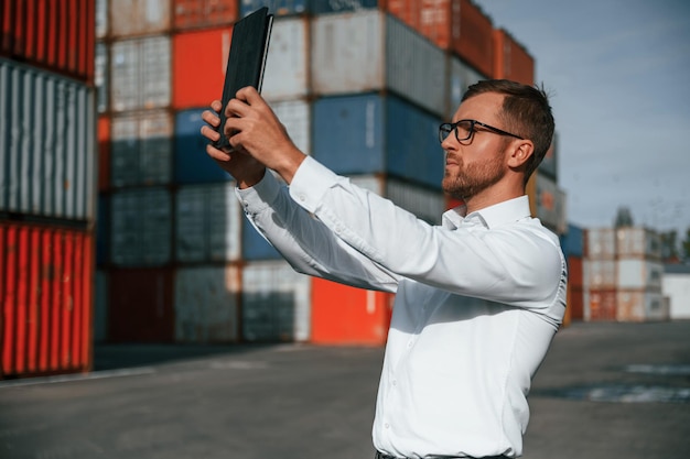 Photo with modern tablet making a photos of objects male worker is on the location with containers