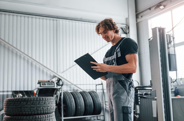 With notepad in hands Adult man in grey colored uniform works in the automobile salon