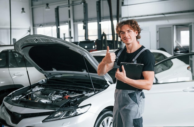 With notepad in hands Adult man in grey colored uniform works in the automobile salon