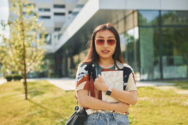 With notepad in hands Young asian woman is outdoors at daytime