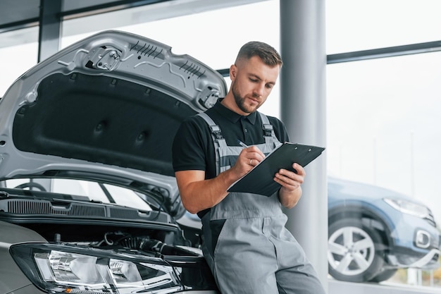 Foto con il taccuino l'uomo in uniforme lavora di giorno nell'autosalone