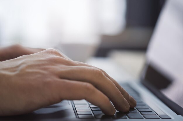 Foto con l'ambiente dell'ufficio sfocato sullo sfondo, l'immagine mostra un primo piano delle mani di un uomo che digitano su un laptop contemporaneo