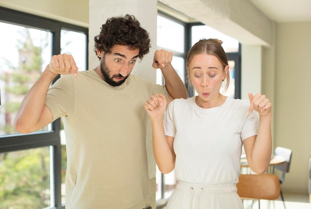 Photo with open mouth pointing downwards with both hands looking shocked amazed and surprised