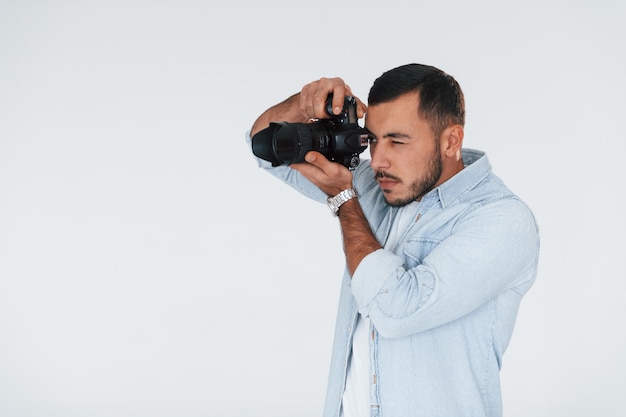 With professional camera Young handsome man standing indoors against white background