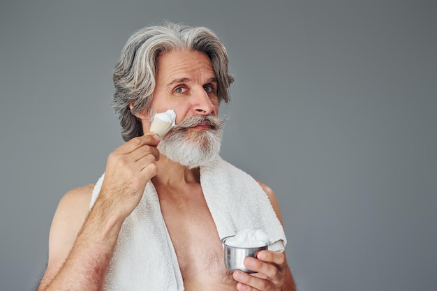 With shaving gel Stylish modern senior man with gray hair and beard is indoors