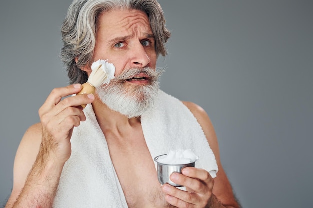 With shaving gel Stylish modern senior man with gray hair and beard is indoors