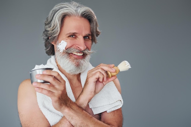 With shaving gel Stylish modern senior man with gray hair and beard is indoors