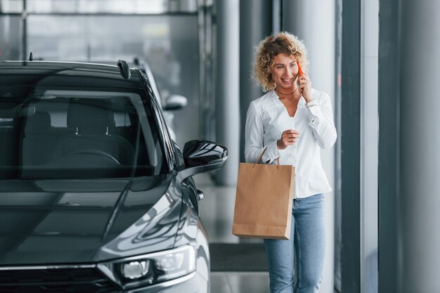 With shopping bag Woman with curly blonde hair is in autosalon