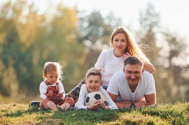 With soccer ball Happy family lying down outdoors near the forest With daughter and son