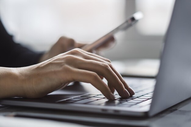 Foto con una scena d'ufficio leggermente sfocata sullo sfondo, l'immagine rivela un primo piano delle mani di una donna che digitano sulla tastiera di un portatile alla moda