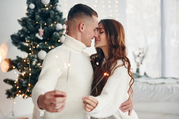 With sparklers in hands Young romantic couple celebrates New year together indoors