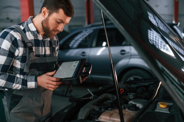 With tablet in hands Man in uniform is working in the auto salon