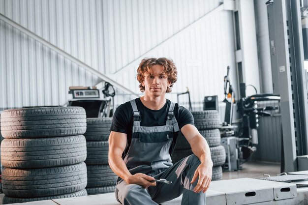 With tool in hand adult man in grey colored uniform works in\
the automobile salon