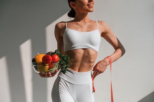 with vegetalbes and fruits young caucasian woman with slim body shape is indoors in the studio