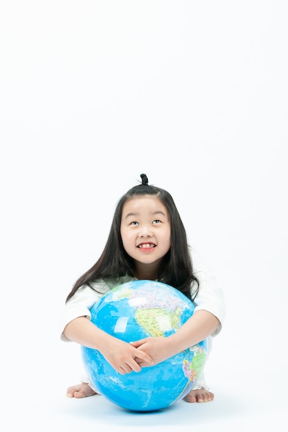 With a white , the child is sitting on a globe and looking at something.