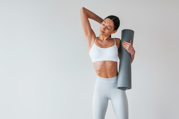 С ковриком для йоги женщина с спортивным стройным телом в нижнем белье, которая находится в студии
