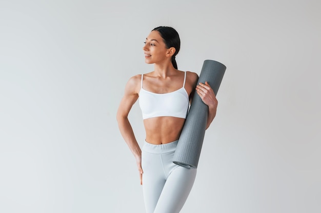 Con tappetino da yoga donna dal fisico snello sportivo in biancheria intima che è in studio