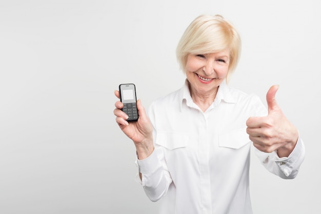 Witharige dame houdt een oude telefoon vast. ze gebruikt het liever in plaats van het kopen en gebruiken van een nieuwe. deze vrouw houdt niet van nieuwe technologieën.