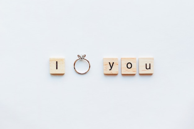 Witte achtergrond met houten woorden I LOVE YOU en diamanten verlovingsring.