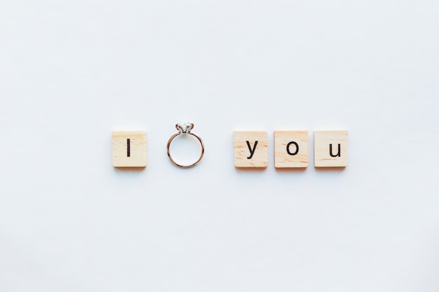 Witte achtergrond met houten woorden i love you en diamanten verlovingsring.