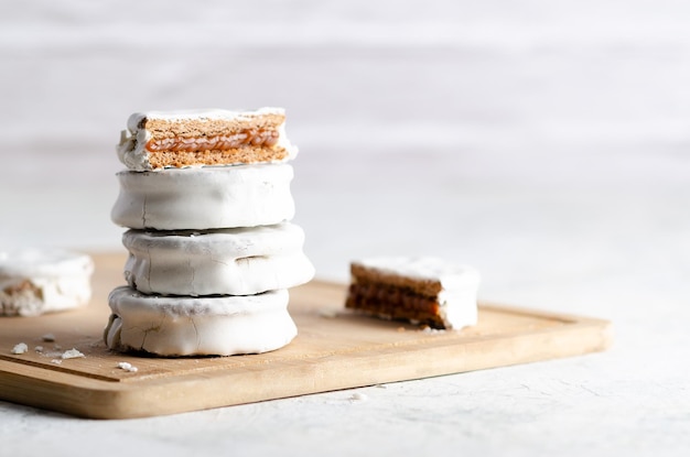 Witte alfajores gevuld met dulce de leche op een houten bord en witte achtergrond.