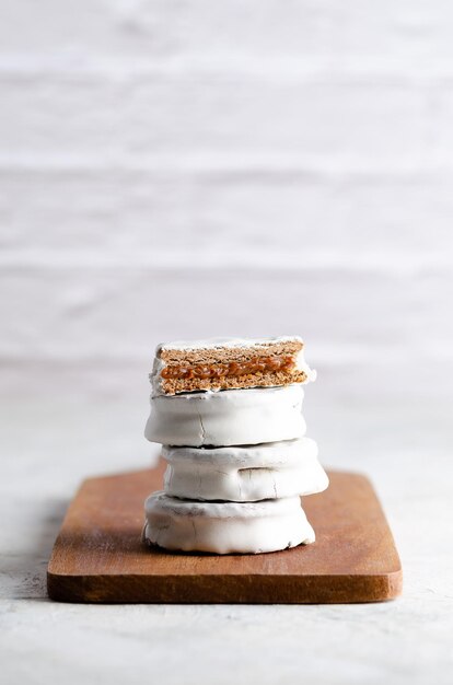 Witte alfajores gevuld met dulce de leche op een houten bord en witte achtergrond.