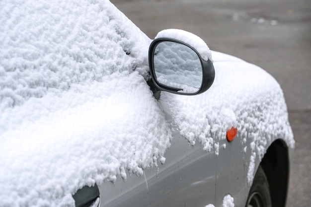 Witte auto is geparkeerd in de buurt van een woongebouw in de stad bedekt met het eerste fragment van de close-up van de herfstsneeuw