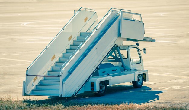 Witte auto met trappen voor passagiersvliegtuigen die het landingsbaangebied van de luchthaven binnenkomen